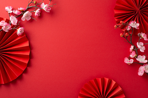 Lunar New Year vibes captured: Overhead shot featuring fans, Feng Shui essentials, and sakura blooms on a crimson backdrop, leaving space for messages or ads