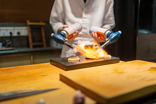 The chef using a spray gun to grill sashimi slices, which is delicious Japanese cuisine.