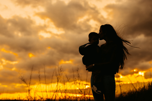 Silhouette of a beautiful young mother holding her son in her arms in the park in autumn.