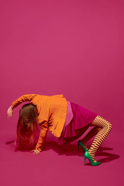 istock Self-expression. Young weird woman in bright clothes posing in extraordinary pose against magenta studio background. 1820505019