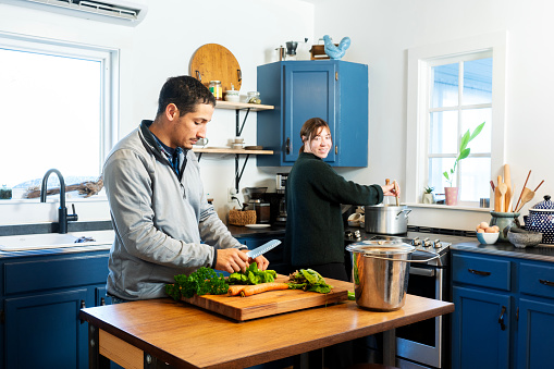 A man separating lettuce leaves for composting instead of throwing it out while his female partner cooks at the stove.