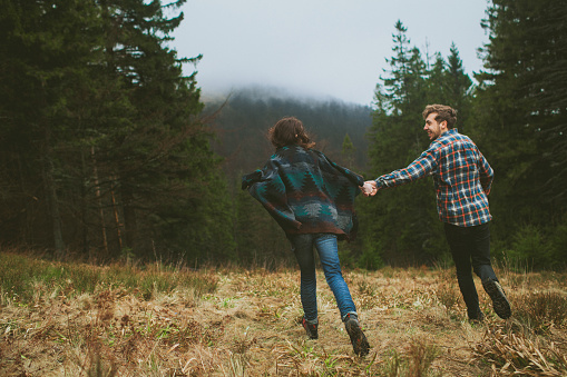 Cheerful couple running holding hands on the meadow in the woods