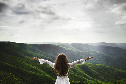 Woman raising arms into the air getting in touch with idyllic nature. She is surrounded with lush green hills
