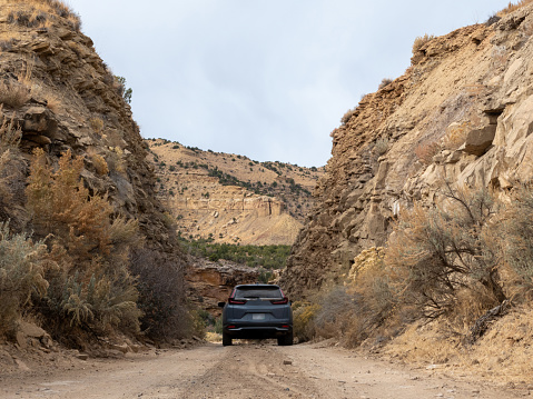 Small SUV on a dirt road in a very narrow road cut between sandstone cliffs.