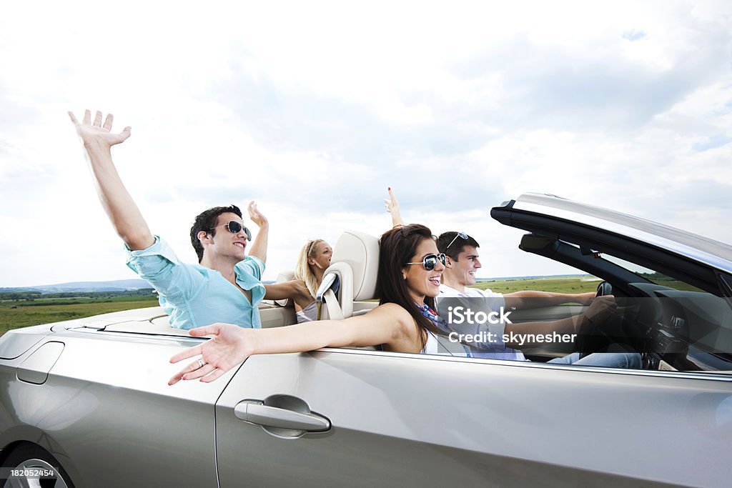 Young couples driving in a cabriolet Side view of four young people with raised hands driving in a Convertible car. Convertible Stock Photo