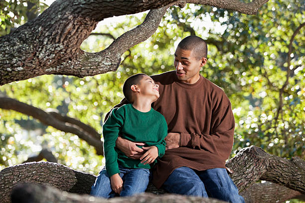 hispânica pai e filho sentado na árvore no parque falando - sc0526 - fotografias e filmes do acervo