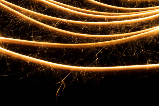 Burning gold sparkler lines on black background as pattern. Christmas festive abstract background for advertising, design, poster, card, flyer.