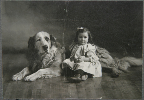 An antique black and white portrait of a little girl and her dog.