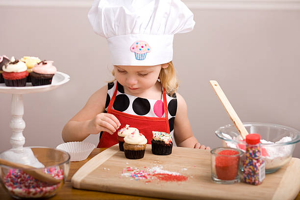 istock Cupcake Decorating by Little Girl in Chef's Hat and Apron 182055109