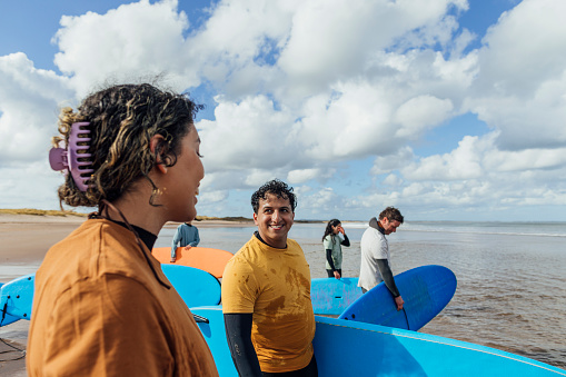 A medium close up side view of surfing students entering the water with their instructor in the North Sea in Ambleside in the North East of England. They're smiling  and looking forward to learning together.