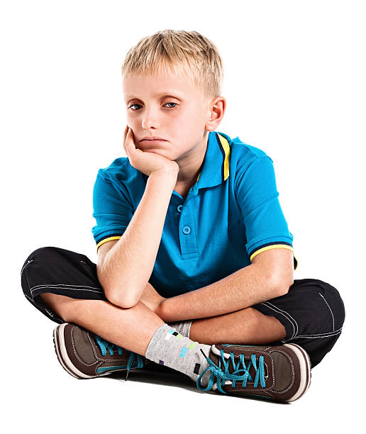 A cheerful boy in a white shirt and jeans sits relaxed on a concrete bench, smiling brightly outdoors. This photo is ideal for promoting children's clothing, lifestyle blogs, and educational materials