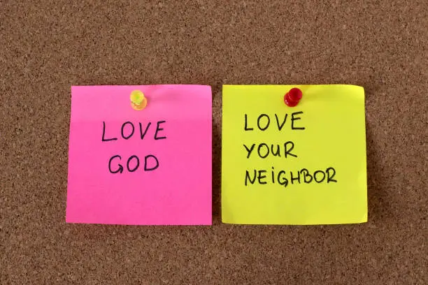 Love God, love your neighbor, handwritten notes on cork pinning board. Christian obedience and faith in Jesus Christ, the greatest commandments from the Bible. Top view.
