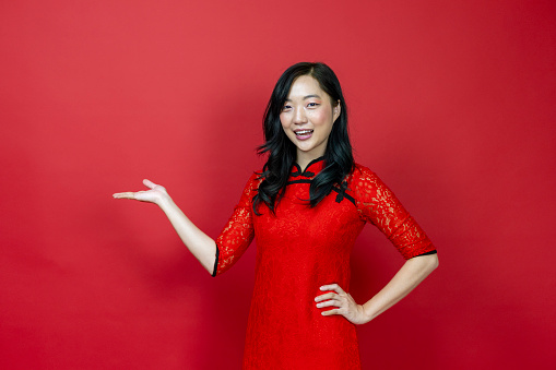 Asian woman with red cheongsam or qipao pointing to present for Chinese New Year celebration holiday isolated on the red background