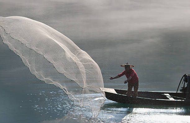 Fisherman on a boat casting out a net stock photo