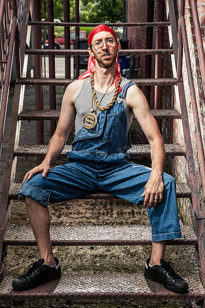 1990s Hip-Hop Goofy Nerd Guy with Bling in Dark Alley "Urban Hip-hop goofy guy from the late 1980s early 1990s with bling sitting on an dirty staircase. He is wearing jeans, bling, a grey wife beater, and a red bandanna." do rag stock pictures, royalty-free photos & images