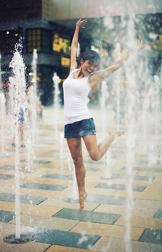 Beautiful young woman jumping in the fountain splashes