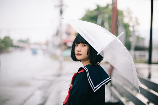 Portrait of Asian school girl walking with umbrella at uraban walkway on raining