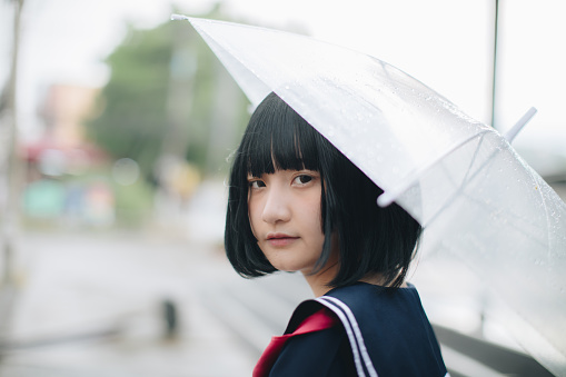 Asian school girl looking with umbrella in urban city