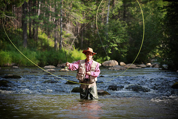 Fly fisherman Fly fisherman stands knee deep in river casting his line. Adobe RGB fly fishing stock pictures, royalty-free photos & images