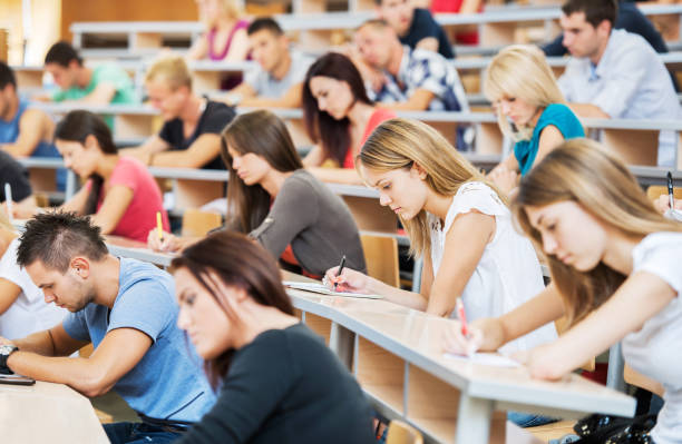 Large group of students writing in notebooks. "Group of college students in the university amphitheatre, they are sitting and doing an exam." continuing education stock pictures, royalty-free photos & images