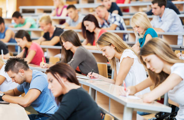 Large group of students writing in notebooks. "Group of college students in the university amphitheatre, they are sitting and doing an exam." exam student university writing stock pictures, royalty-free photos & images