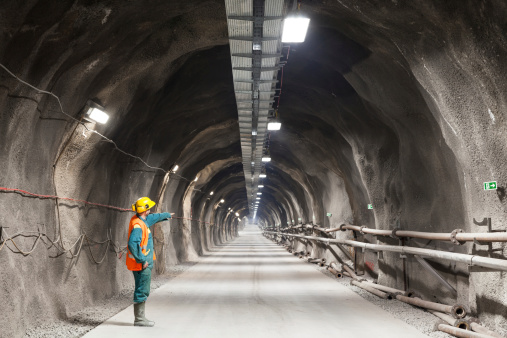 Professional underground workerpointing downward in a tunnel/mine.