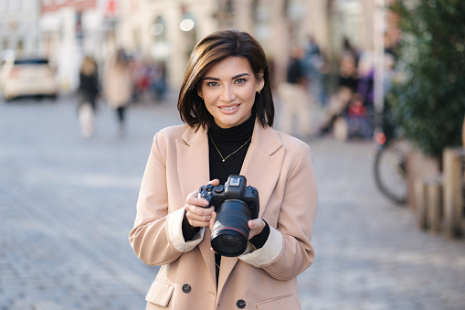 Close-up portrait of professional female photographer hold mirrorless camera. Attractive young woman look into camera