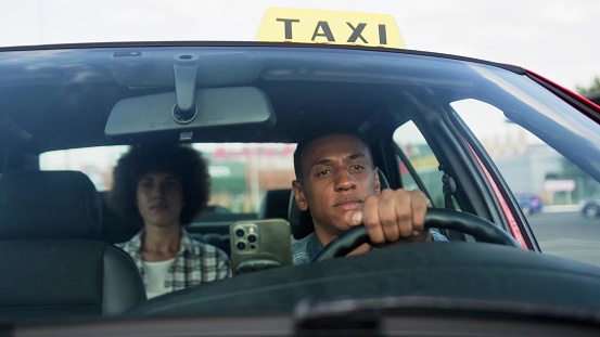 African American taxi driver driving with woman on the backseat. Yellow taxi car roof sign. People, job, service concept. Slow motion