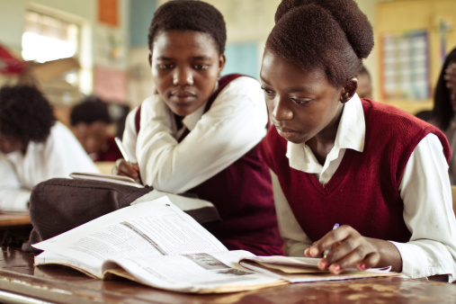 South African girls (from the Xhosa tribe) working together  on their studies at an old worn desk in a class room in the Transkei region of rural South Africa.