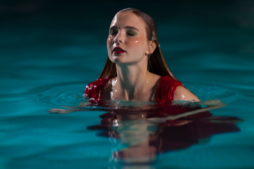 A portrait of a woman in a red dress at night time in a swimming pool.