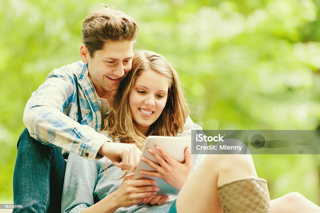 Couple in Green Nature with Tablet PC Modern Technology young couple sitting on the green grass, enjoying a perfect summer day together in nature, playing with their tablet pc. Adult Stock Photo