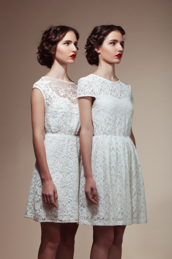 Studio portrait of two beautiful twins in white dresses. Professional make-up and hairstyle.