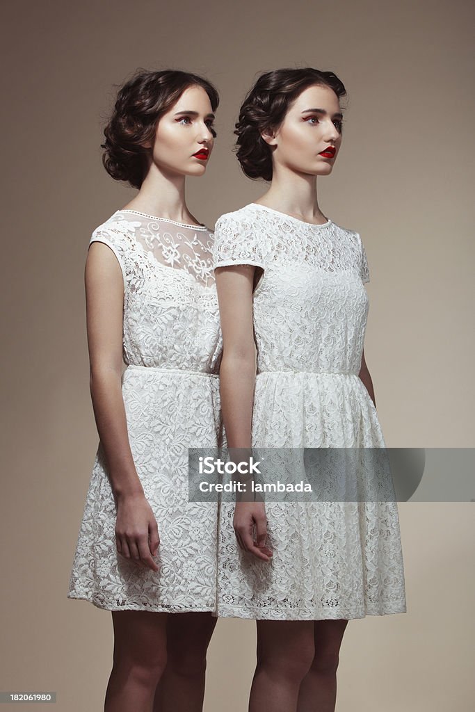 Beautiful twins Studio portrait of two beautiful twins in white dresses. Professional make-up and hairstyle. Twin Stock Photo