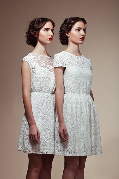 Beautiful twins Studio portrait of two beautiful twins in white dresses. Professional make-up and hairstyle. twin photos stock pictures, royalty-free photos & images