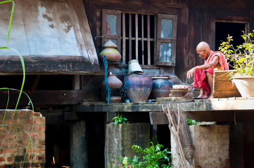 A Burmese monk in his 70s, sitting outside his monastery where he is washing dishes, in Mandalay, Myanmar