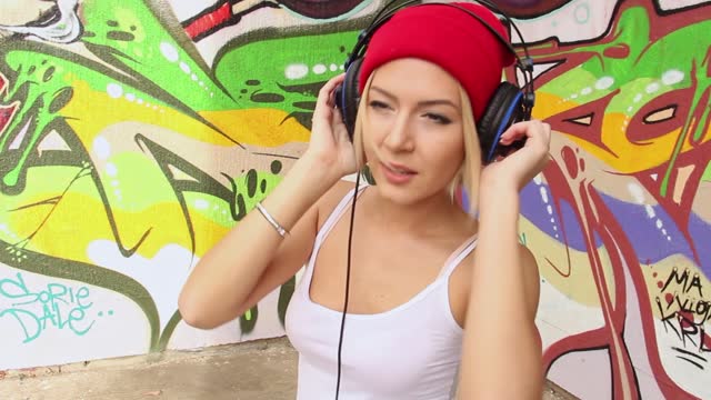 Urban Young Woman Dancing While Listening To Music Via Headphones In Front Of A Graffiti Wall