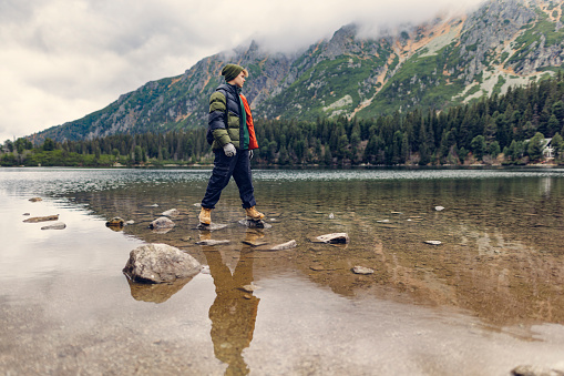 Family is hiking in the High Tatra Mountains, Slovakia. Teenage boy is walking on the stones in the Popradské pleso lake. Cold and overcast autumn day.
Shot with Canon R5