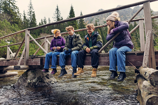 Family is hiking in the High Tatra Mountains, Slovakia. Family is sitting on a bridge over a mountain river. Cold and overcast autumn day.
Shot with Canon R5