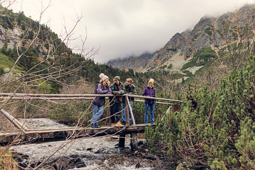 Family is hiking in the High Tatra Mountains, Slovakia. Family is sitting on a bridge over a mountain river. Cold and overcast autumn day.
Shot with Canon R5