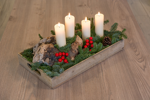 An example of a hand-made Advent or Christmas composition with four burning candles, on an old tree trunk, surrounded by green spruce branches and red berries. Advent, Christmas and New Year concept.