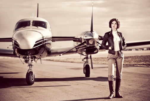 Horizontal portrait of a young woman dressed in 40's aviator attire stands on the run way with her plane.Image is processed from a 16 bit RAW file and profiled in ProPhoto RGB. All my images are professionally retouched.**Need more shots from this series: