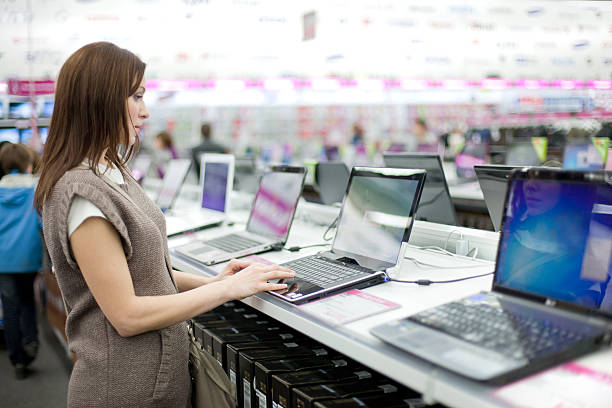 mujer elige la computadora portátil - tienda de electrónica fotografías e imágenes de stock