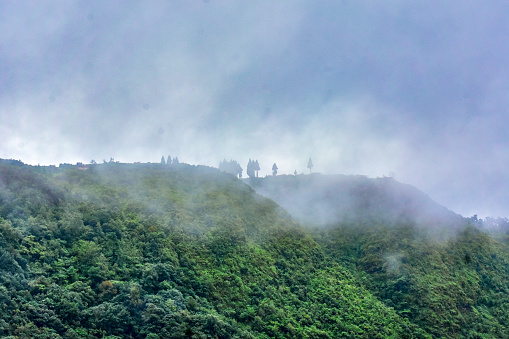 Fogs at the top of a mountain covered in green vegetation.