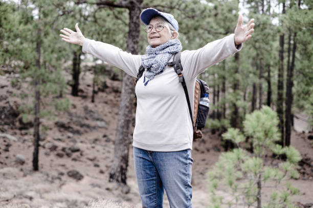 istock Active senior woman holding backpack standing in the pine forest with open arms enjoying nature and adventure. Sport and healthy lifestyle concept 1820675959