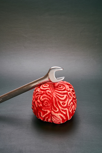 Wrench on top of a red human brain with a dark background, concept of breaking mental barriers