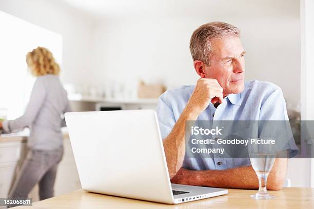 Homem Pensativo Com Laptop Enquanto Mulher Cozinhar Na Cozinha - Fotografias de stock e mais imagens de Interior de Casa