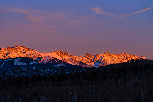 Alpenglow Vail Colorado Mountains - Gore Range mountains bathed in warm alpenglow light in early winter with snowcapped peaks. Warm and cool complementary colors in scenic majestic mountain landscape. Vail, Colorado USA.