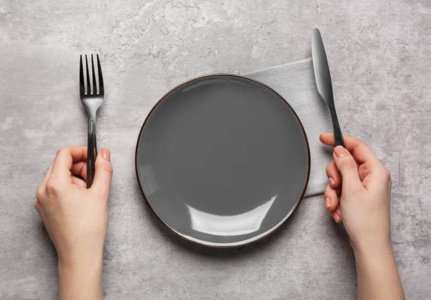 istock Woman with empty plate and cutlery at light grey table, top view 1820706804