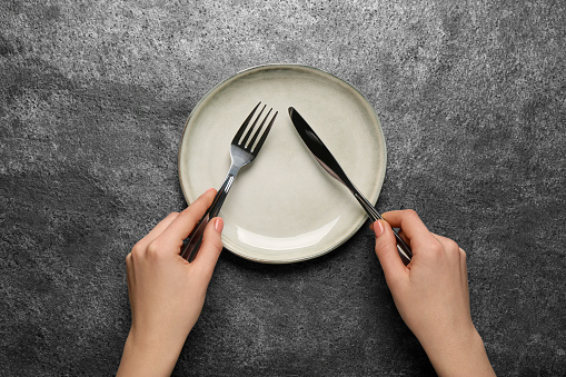 Woman with empty plate and cutlery at grey table, top view