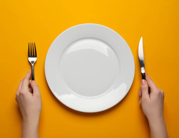 istock Woman with empty plate and cutlery on orange background, top view 1820706874